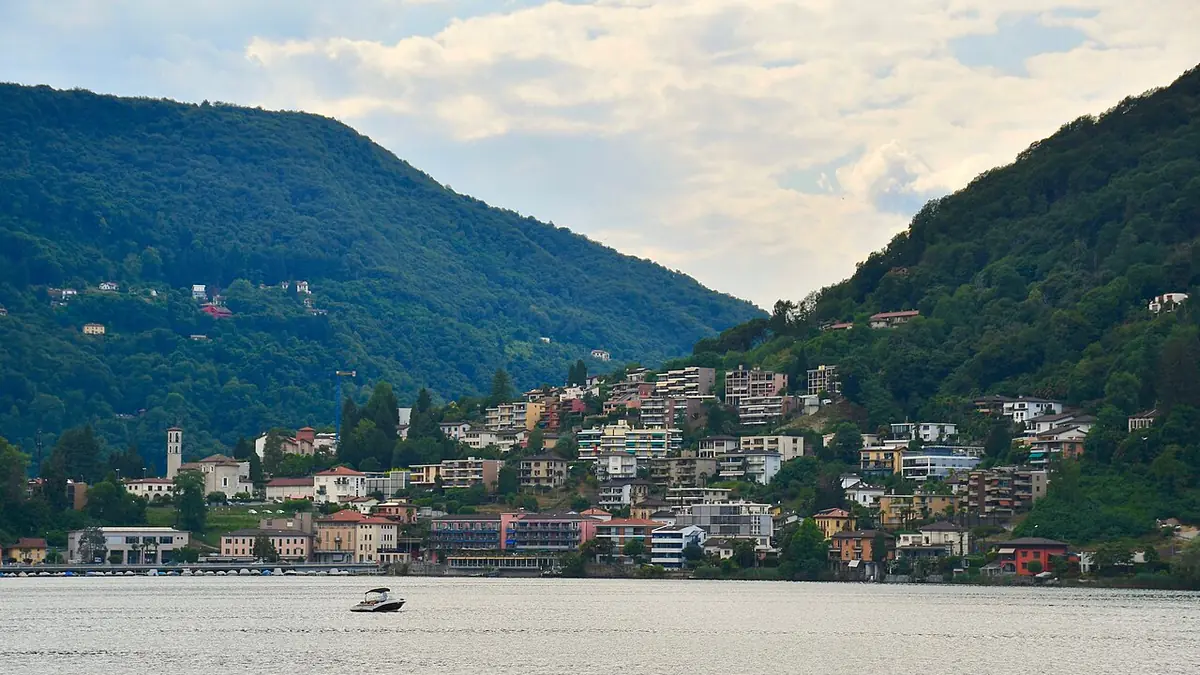 Vue de la vallée Mendrisio-Como à la frontière Tessin-Lombardie, avec architecture alpine suisse et constructions italiennes, forêts et lac au loin.